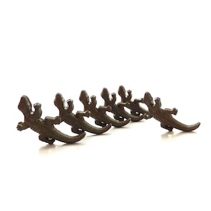May include: A set of six brown plastic toy lizards in a line, all facing the same direction. The lizards are in a running pose with their tails extended.