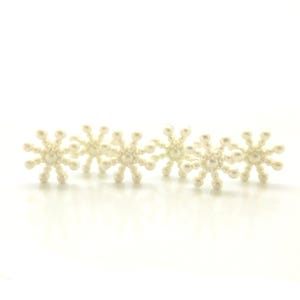 May include: Five white pearl snowflake embellishments. Each snowflake is made of small white pearls arranged in a starburst pattern.