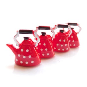 Puede incluir: Cuatro tetera roja en miniatura con lunares blancos y asas plateadas. Las teteras están alineadas en una fila sobre una superficie blanca.