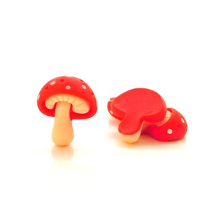 May include: Three red mushroom-shaped decorative objects with white polka dots. One mushroom stands upright, while the others are lying down. The stems are beige, and the caps are a vibrant red.