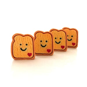 May include: Four small, orange, smiling toast-shaped figurines with red hearts. Each figurine has a different facial expression.
