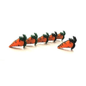 May include: Six orange carrot shaped buttons with green tops. The buttons are arranged in a line, with one button slightly offset from the others.