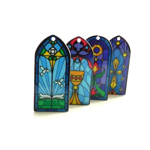 May include: Four stained glass window ornaments with different religious symbols. The ornaments are blue, green, yellow, red, and purple.