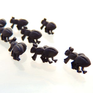 May include: A group of eight black plastic ant figurines, arranged in a line on a white surface.