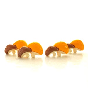May include: Five plastic mushroom-shaped toys in a row. The mushrooms are brown and yellow with a rounded top and a stem.