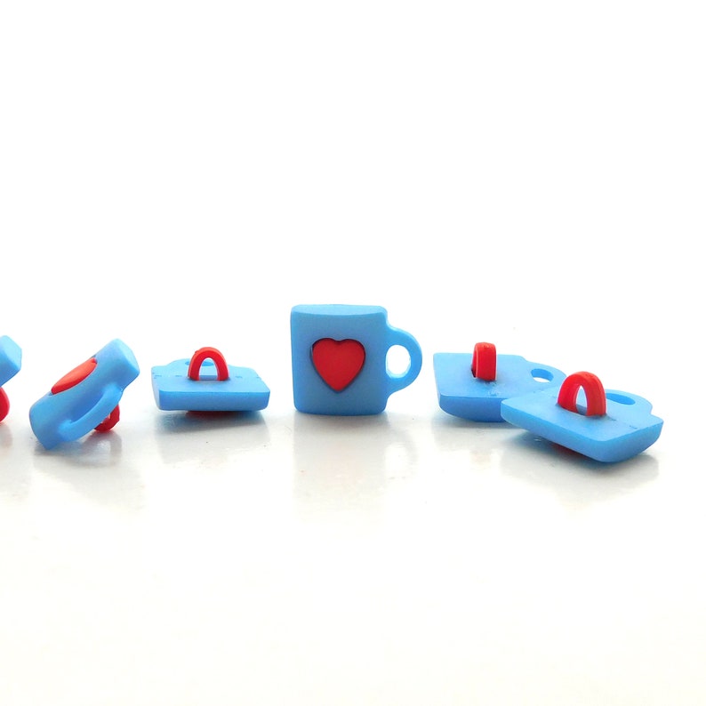 May include: A collection of light blue buttons with red accents. The buttons include a mug with a red heart, and other buttons with a handle. The buttons are arranged on a white surface.