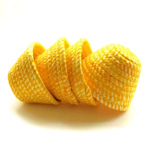 May include: A stack of four yellow woven baskets with a white and yellow checkered pattern. The baskets are cone-shaped and have a white trim around the top edge. The baskets are arranged in a curved line.