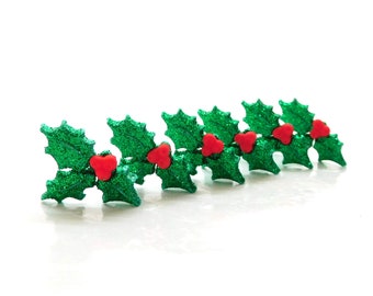 May include: Six glittery green holly leaf decorations with red berry accents are arranged in a row. The leaves have a textured, sparkling finish, and the berries are a bright red. Ideal for festive crafts and seasonal decorations.
