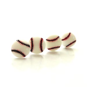 May include: Four small, round, white baseball-themed spheres arranged in a row. Each sphere features the characteristic red stitching pattern of a baseball, with black thread details running across the smooth, off-white surface of the objects.
