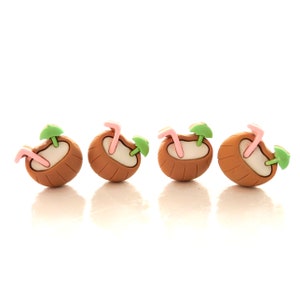 May include: Four brown coconut-shaped drink holders with pink straws and green palm tree umbrellas.