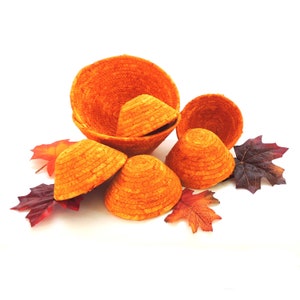 May include: A set of six orange woven baskets of varying sizes, arranged on a white surface with fall leaves.