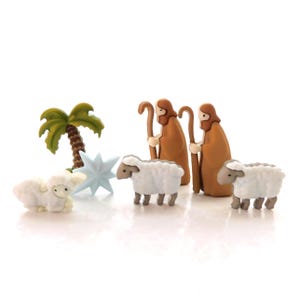 May include: A set of Christmas nativity scene figurines, including two brown-robed shepherds with staffs, a blue star, a palm tree, and three white lambs.