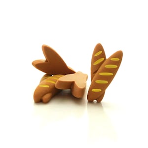 May include: Four brown and yellow plastic toy baguettes. The baguettes are arranged in a pile.