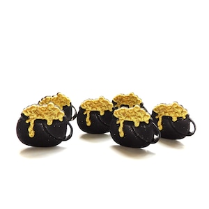 May include: Six black cauldron charms with gold glitter bubbling over the top. Each cauldron has a small black handle. The charms are arranged on a white background.