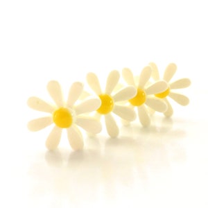 May include: A row of four daisy-shaped embellishments, each featuring eight white petals surrounding a smooth, raised, glossy yellow center. The flowers are arranged in a line, showing a consistent design with a bright, clean color palette.