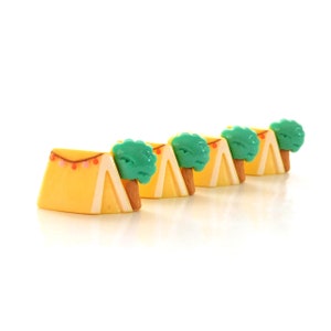 May include: Five miniature yellow and white tents with green trees on top. The tents are lined up in a row.