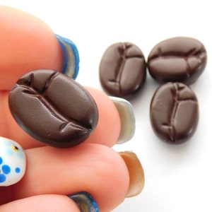 May include: Four brown ceramic coffee bean shaped buttons. The buttons are oval shaped with a raised line down the center.