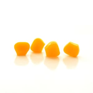 May include: Four bright yellow gummy candies in the shape of a diamond, arranged in a row on a white surface.