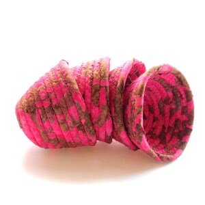 May include: A stack of four pink and brown fabric baskets. The baskets are cone-shaped and have a stitched, textured appearance. The pink color is vibrant, and the brown adds a contrasting pattern. The baskets are arranged on a white background.