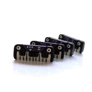 May include: Four miniature black and white piano key charms with a dark blue top. The charms are arranged in a row, each with a unique design of circles and lines. The keys are white and the body is black.