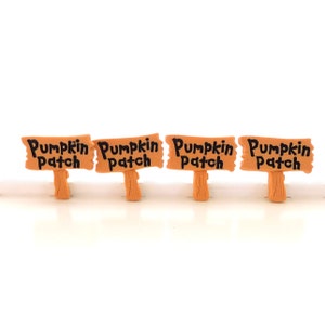 K&ouml;nnte beinhalten: Vier kleine Holzschilder mit dem Text "Pumpkin Patch" in Schwarz auf hellbraunem Hintergrund. Die Schilder sind in einer Reihe auf einer wei&szlig;en Oberfl&auml;che angeordnet.