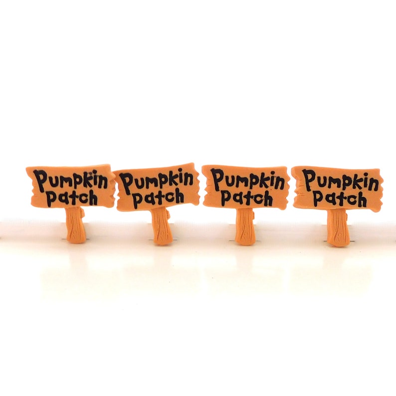 K&ouml;nnte beinhalten: Vier kleine Holzschilder mit dem Text "Pumpkin Patch" in Schwarz auf hellbraunem Hintergrund. Die Schilder sind in einer Reihe auf einer wei&szlig;en Oberfl&auml;che angeordnet.