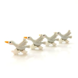 May include: Four gray ceramic geese flying in a row with orange beaks and white clouds beneath them.