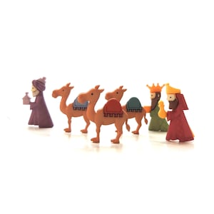 May include: A set of miniature figurines representing the Three Wise Men and their camels. The camels are tan with colourful saddle blankets. The Wise Men wear robes in purple, green, and red, with gold crowns and holding gifts.