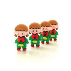 May include: Four small, colorful figurines of cartoon characters. Each figure has a brown hairstyle, a red bow tie, a green outfit, and red shoes. The figures are arranged in a row against a white background.
