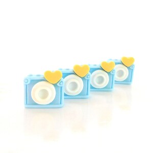 May include: Four blue and white camera shaped erasers with yellow heart accents.
