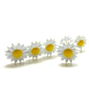 May include: A collection of five small daisy-shaped buttons, each featuring a bright yellow center surrounded by white petals. The buttons are arranged in a staggered formation, showcasing their uniform floral design and smooth, matte finish.