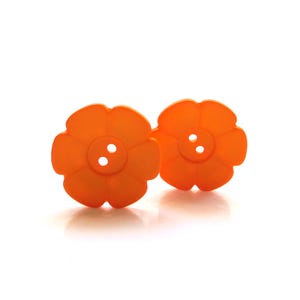 以下が含まれることがあります： オレンジ色の花の形をしたボタンが2つ。それぞれに3つの穴があります。ボタンは、しっかりとした不透明な素材でできており、白い背景に配置されています。ボタンは明るく陽気な色で、さまざまな縫製プロジェクトに適しています。