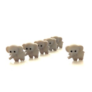 May include: Six white elephant buttons with black eyes. The buttons are arranged in a line, with the last button slightly offset from the others.