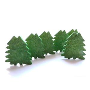 May include: A collection of small, green, wooden Christmas tree figurines. Each tree has a detailed, textured surface and a classic evergreen shape. The trees are arranged in a slightly curved line against a white background, suggesting a miniature forest.