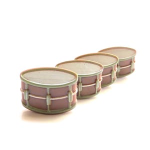 Puede incluir: Cuatro tambores en miniatura de cerámica en fila, cada uno con un acabado verde y marrón. Los tambores están dispuestos del más grande al más pequeño, con el tambor más grande en la parte posterior y el tambor más pequeño en la parte delantera.