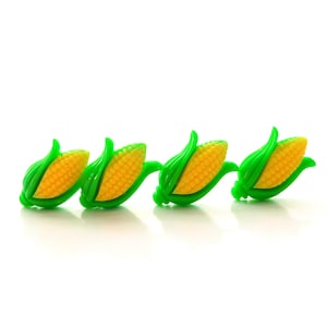 May include: Three small plastic corn on the cob decorations. Each corn is yellow with green husks. The corn is arranged in a row.