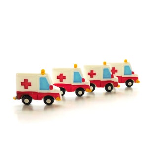 May include: Four miniature toy ambulances lined up in a row. Each ambulance is white with red crosses and blue accents. The ambulances are made of plastic and have wheels.