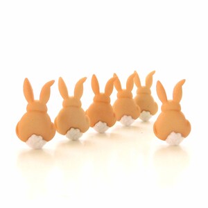 May include: Six brown bunny-shaped cookies with white frosting on the back, arranged in a row on a white surface.