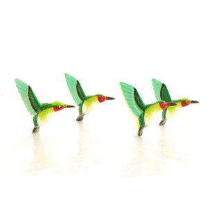 May include: Four green and blue hummingbirds with red beaks are in flight. The hummingbirds are made of wood and are painted in bright colors.