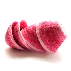 May include: A stack of four pink woven baskets with a light pink trim. The baskets are arranged in a row, with the openings facing the same direction. The baskets have a zig-zag stitch pattern.