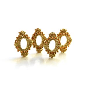 May include: Four ornate, gold-colored decorative frames with an oval opening in the center. The frames have a detailed, textured design with small, orange-colored accents. They are arranged in a row against a white background.