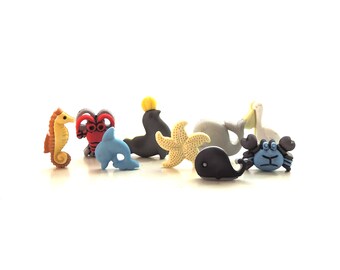 May include: A set of eight colorful plastic sea creature buttons. The buttons feature a seahorse, a lobster, a dolphin, a penguin, a starfish, a whale, a crab, and a seal. The buttons are perfect for adding a touch of whimsy to any craft project.