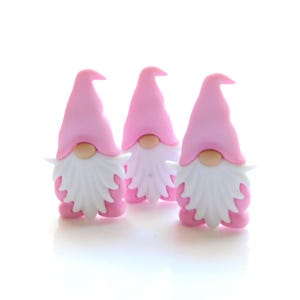 May include: Three pink gnomes with white beards. The gnomes are made of a soft, pliable material and have a whimsical, charming appearance.