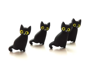 May include: Four black cat figurines with yellow eyes. The cats are in a row, facing forward, with their tails curled behind them.