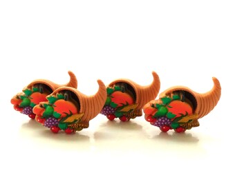 May include: Four miniature cornucopia figurines. Each horn of plenty is tan with a curved shape, filled with a variety of colorful fruits and vegetables, including pumpkins, grapes, and corn. The figurines are set against a white background.
