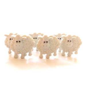 Peut inclure: Un groupe de six figurines de moutons en plastique blanc avec des yeux noirs et une surface texturée. Les moutons sont disposés en rangée, face avant.
