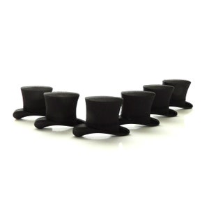 May include: Six black top hats arranged in a row on a white background. The hats are all the same size and shape, and they are all facing the same direction.