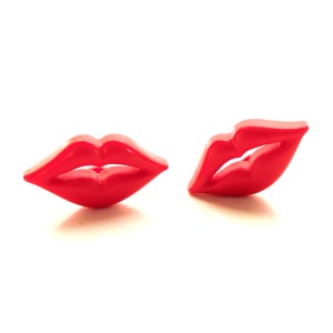 May include: Two bright red lip-shaped objects are displayed against a white background. The objects are glossy and appear to be made of plastic or a similar material. The lips are slightly parted, suggesting a kiss.