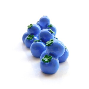 May include: A cluster of blue blueberries with green leaves, arranged in a pile on a white background.