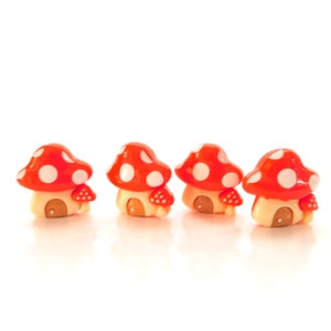May include: Four miniature mushroom houses. Each has a red cap with white spots, a tan base, a small brown door, and tiny red mushroom accents. The background is white.